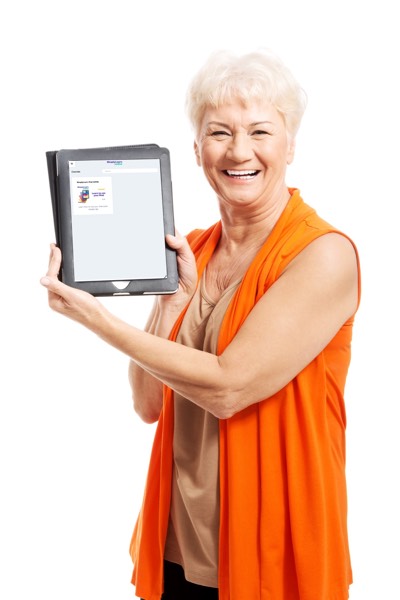 Cheerful senior woman with short white hair and an orange top, smiling broadly while holding up a tablet with a blank screen toward the camera against a white background.