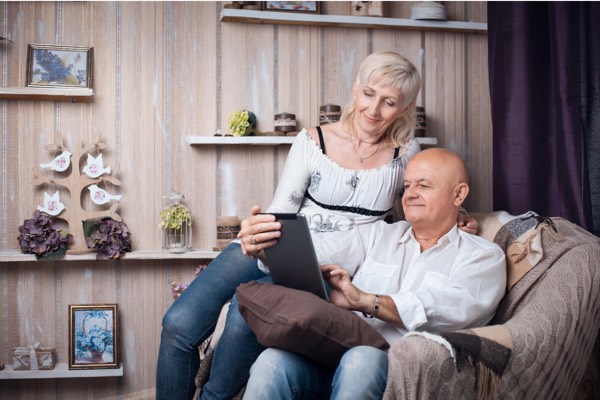 Affectionate senior couple relaxing on a couch in a cozy home, smiling while looking at a tablet screen together.